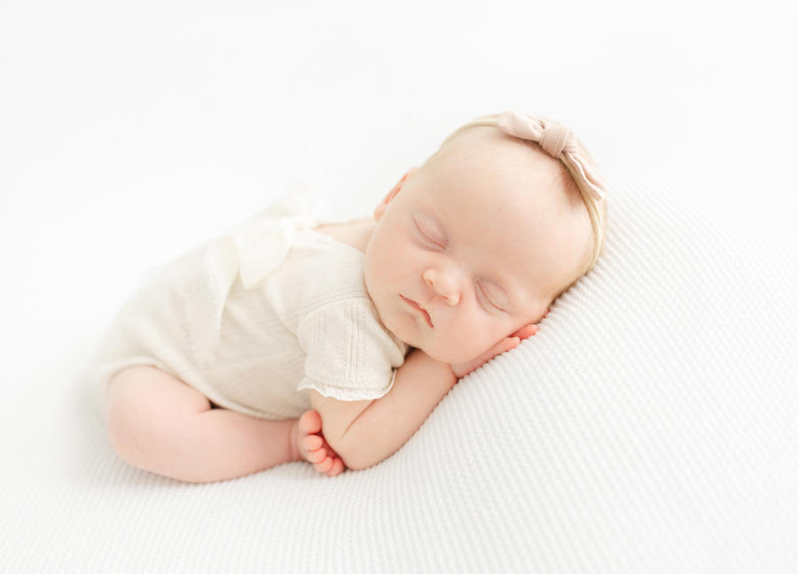 a newborn baby posed on a white blanket with her feet touching her elbows