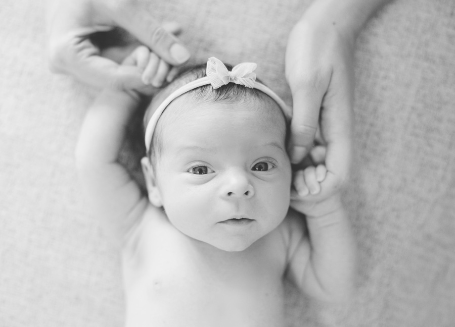 A black and white image of a newborn girl with a headband holding on to her mother's hands