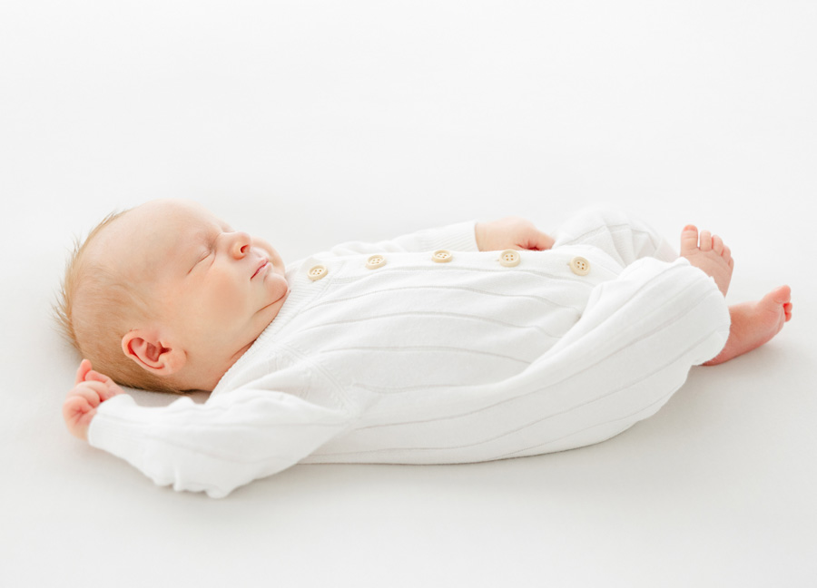 A baby boy in a white onesie sleeping on a beanbag 