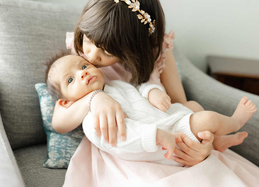 little girl giving her newborn sister a kiss