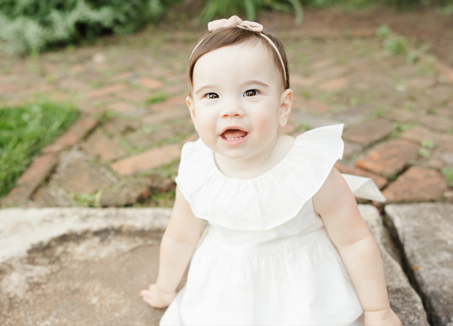 A one year old little girl in a white dress sitting on a stoop at historic Oatlands in Leesburg during their family photoshoot