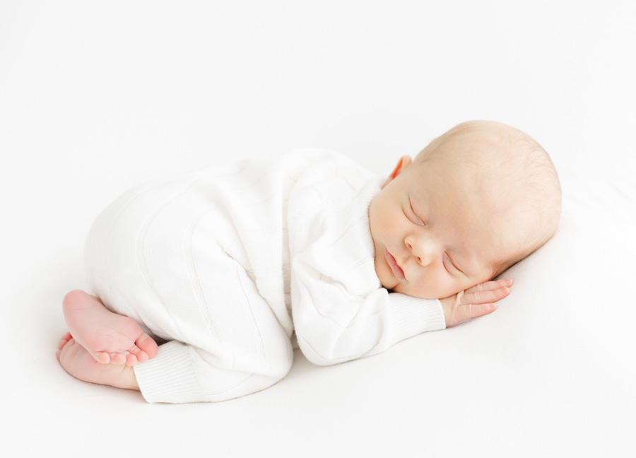 Here is an SEO-friendly, descriptive alt tag that aligns with your brand and target keywords:
Alt text:
Newborn baby boy peacefully sleeping on his side in a soft white outfit on a clean white backdrop, captured during a timeless in-studio newborn photography session by Northern Virginia newborn photographer Stephanie Honikel.