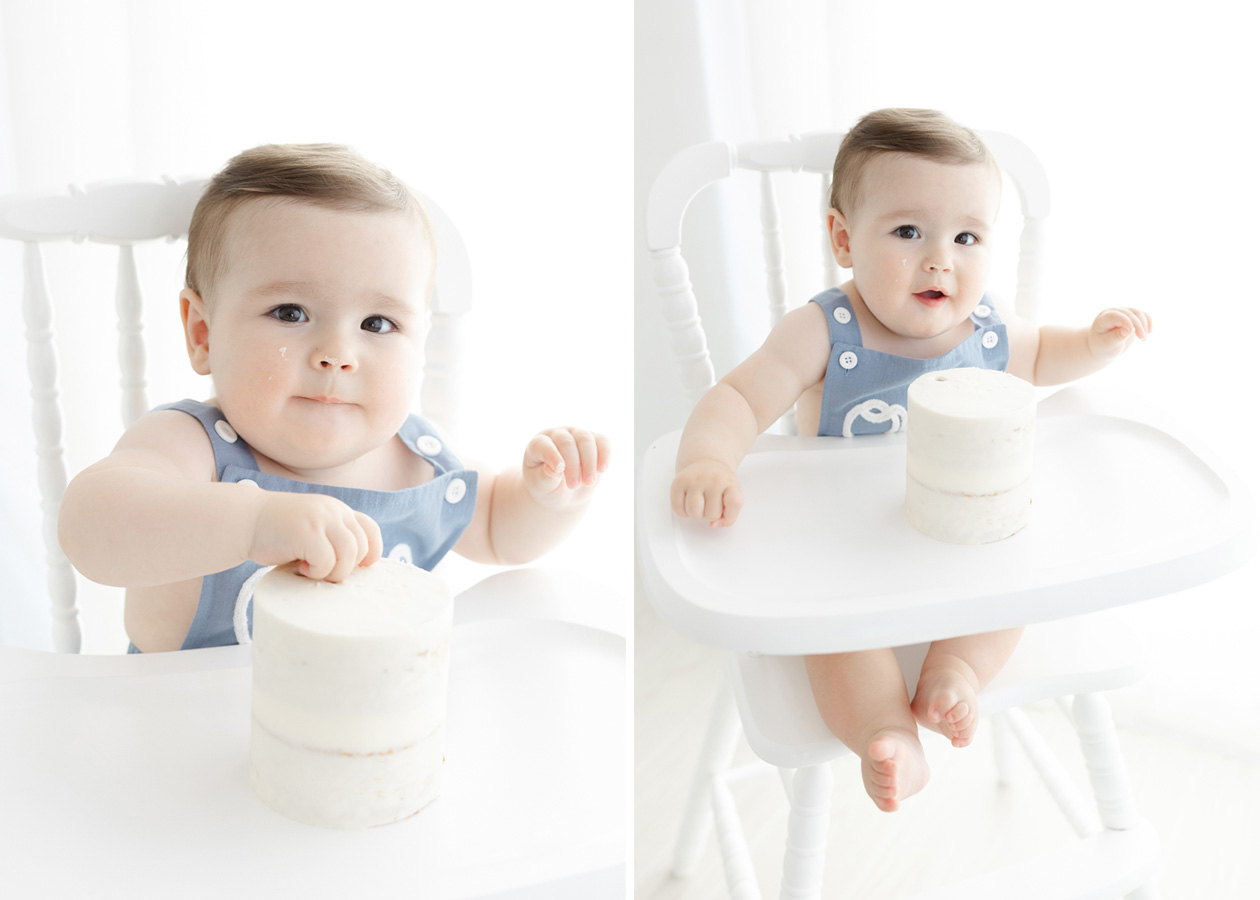 One-year-old baby boy in a blue romper sits in a white high chair exploring his birthday cake during a Northern Virginia cake smash photography session. The two images capture his curious expressions and first touches of the simple white cake.