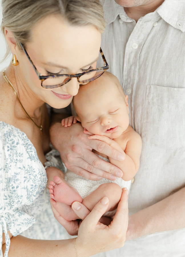 Mother and father lovingly holding their sleeping newborn baby during a light and natural studio newborn session.