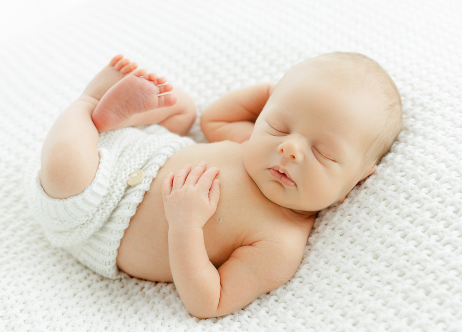 Sleeping newborn baby posed naturally on a soft white knitted blanket, a timeless example of newborn photos ideas Northern Virginia.