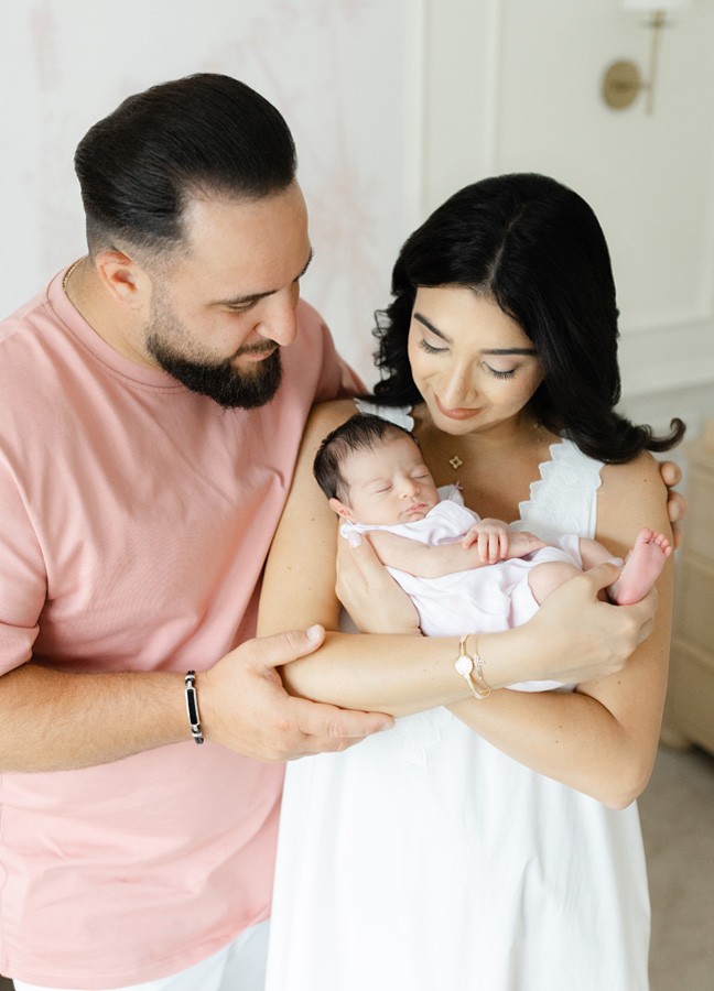 Mother and father smiling down at their sleeping newborn daughter during a natural light Northern Virginia newborn photography session.